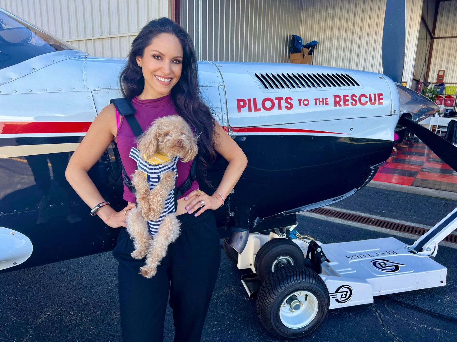 Cheryl Martinez holding a small dog beside a Pilots To The Rescue aircraft
